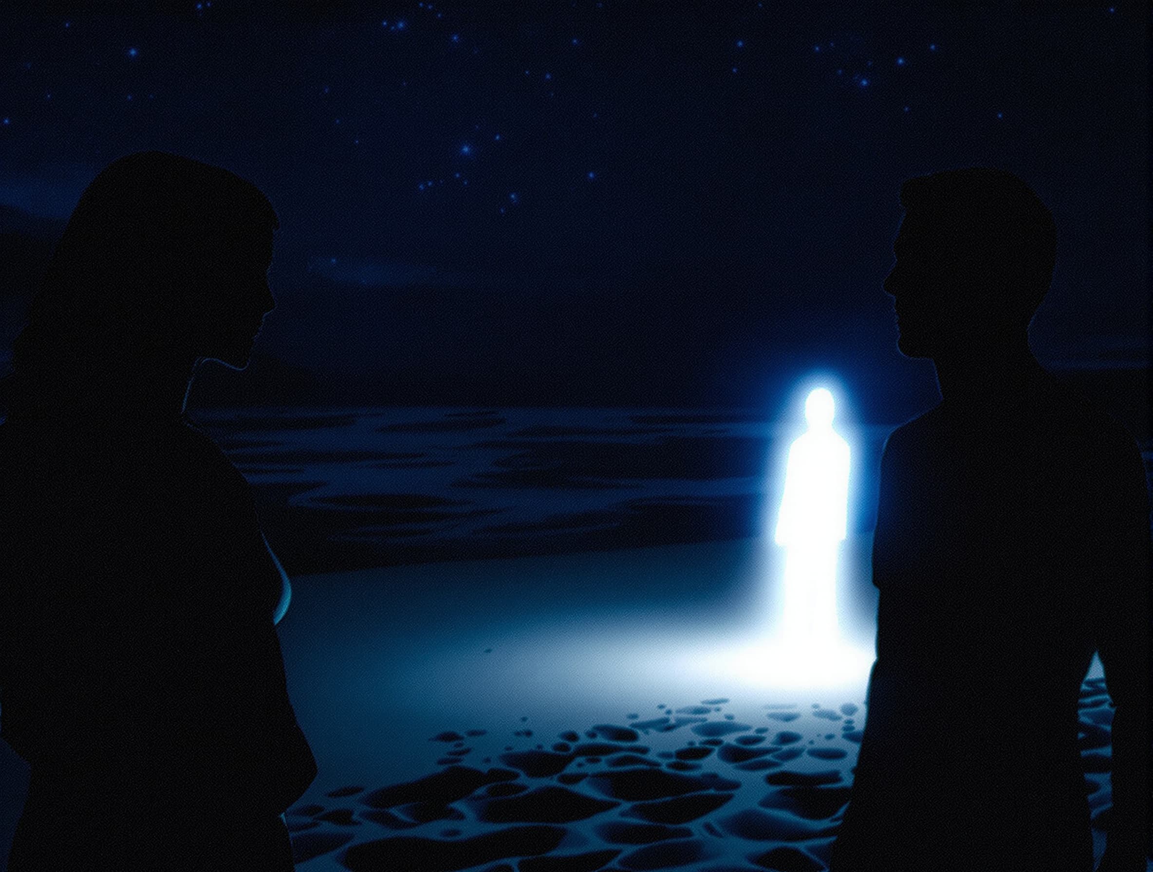 A digital art image shows a dark silhouette of a woman on the left side of the frame, and a blurred silhouette of a man on the right side of the frame, both standing on a beach. The man on the left is facing the glowing man. The glowing man is emitting a bright white light that illuminates the sand around him. The ocean is in the background, and the sky is a dark blue with stars. The image has a grainy texture. The color palette is mostly blues and whites, with some oranges and yellows in the sky.