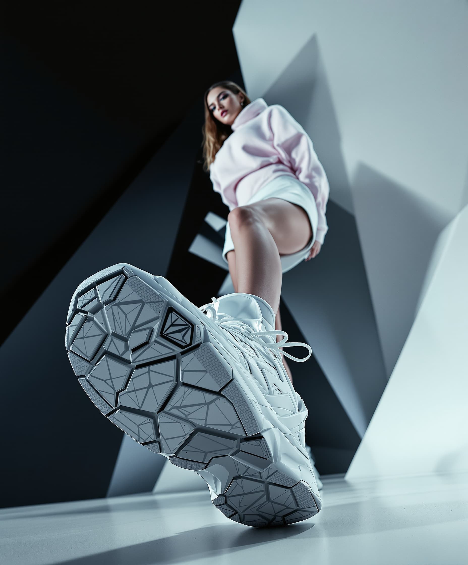 Model leaning towards the camera, low angle, ultra wide angle lens, one leg extended towards the camera, sneaker in focus, dynamic editorial pose, futuristic white tracksuit made of a sweater and a short tennis skirt, Deep studio lighting, contrasts, geometric background, fashion magazine style. Glamorous photorealism.